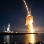 A long-exposure photograph of NASA's Space Launch System (SLS) rocket launching the Artemis II mission into a starry night sky, with a bright orange light trail over a body of water and the text "Artemis II Launch" in the corner.