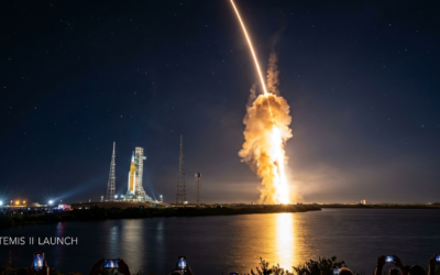 A long-exposure photograph of NASA's Space Launch System (SLS) rocket launching the Artemis II mission into a starry night sky, with a bright orange light trail over a body of water and the text "Artemis II Launch" in the corner.